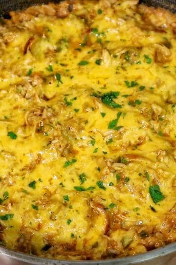 A skillet filled with cheesy buffalo chicken and rice, topped with melted cheddar cheese and herbs.