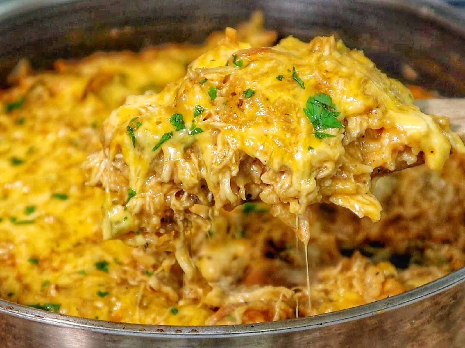 A skillet filled with cheesy buffalo chicken and rice, topped with melted cheddar cheese and herbs.