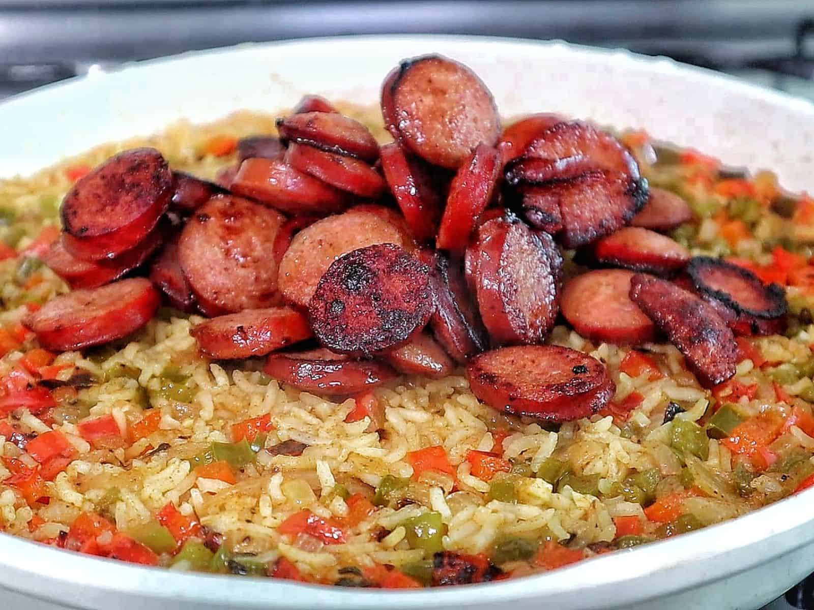 Honey garlic sausage and rice in a skillet with browned sausage slices, seasoned rice, bell peppers, and fresh parsley garnish.