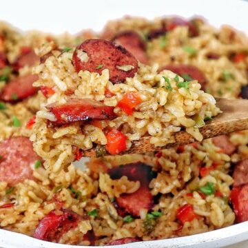 Honey garlic sausage and rice in a skillet with browned sausage slices, seasoned rice, bell peppers, and fresh parsley garnish.