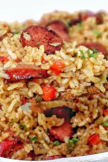 Honey garlic sausage and rice in a skillet with browned sausage slices, seasoned rice, bell peppers, and fresh parsley garnish.