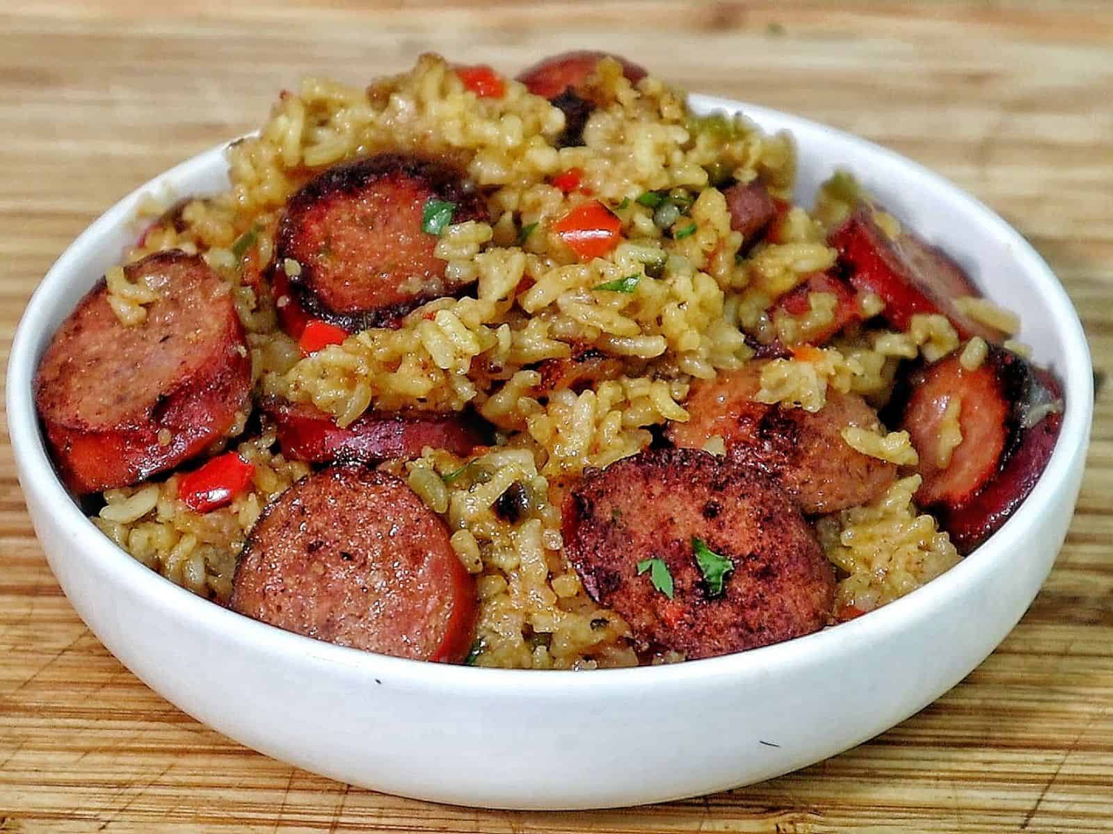 Honey garlic sausage and rice in a skillet with browned sausage slices, seasoned rice, bell peppers, and fresh parsley garnish.