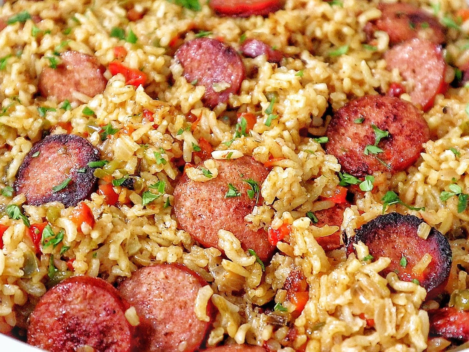 Honey garlic sausage and rice in a skillet with browned sausage slices, seasoned rice, bell peppers, and fresh parsley garnish.