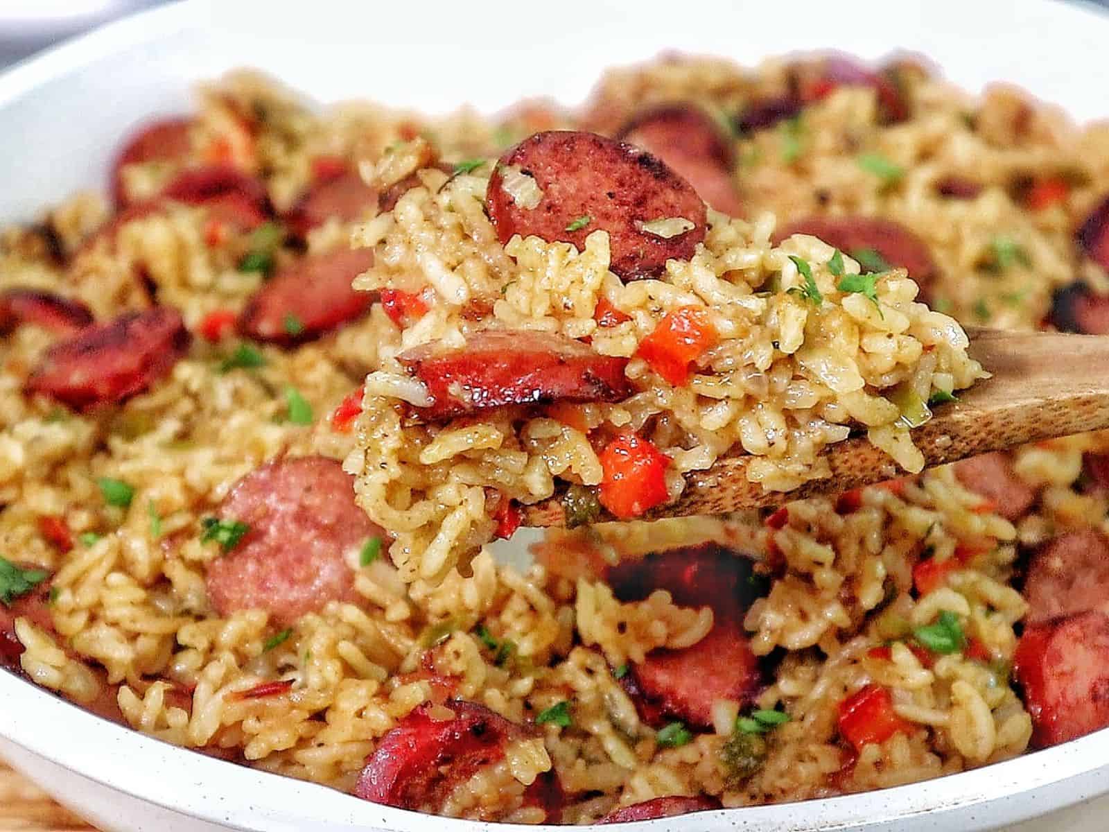 Honey garlic sausage and rice in a skillet with browned sausage slices, seasoned rice, bell peppers, and fresh parsley garnish.