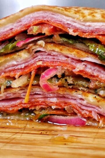 Toasted Italian sub wrap sliced in half, filled with layers of ham, salami, pepperoni, melted provolone cheese, lettuce, tomatoes, onions, and banana peppers.