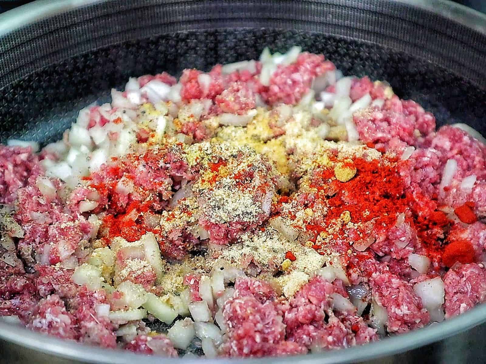 Ground beef and chopped onions in a slow cooker, seasoned with spices for cooking.