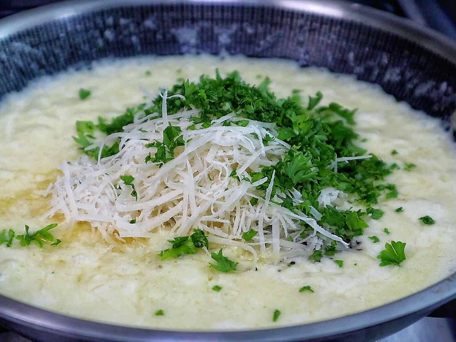 A thick slice of garlic parmesan meatloaf topped with a creamy garlic parmesan sauce and fresh parsley, served on a wooden cutting board with a juicy, tender center visible in every bite.