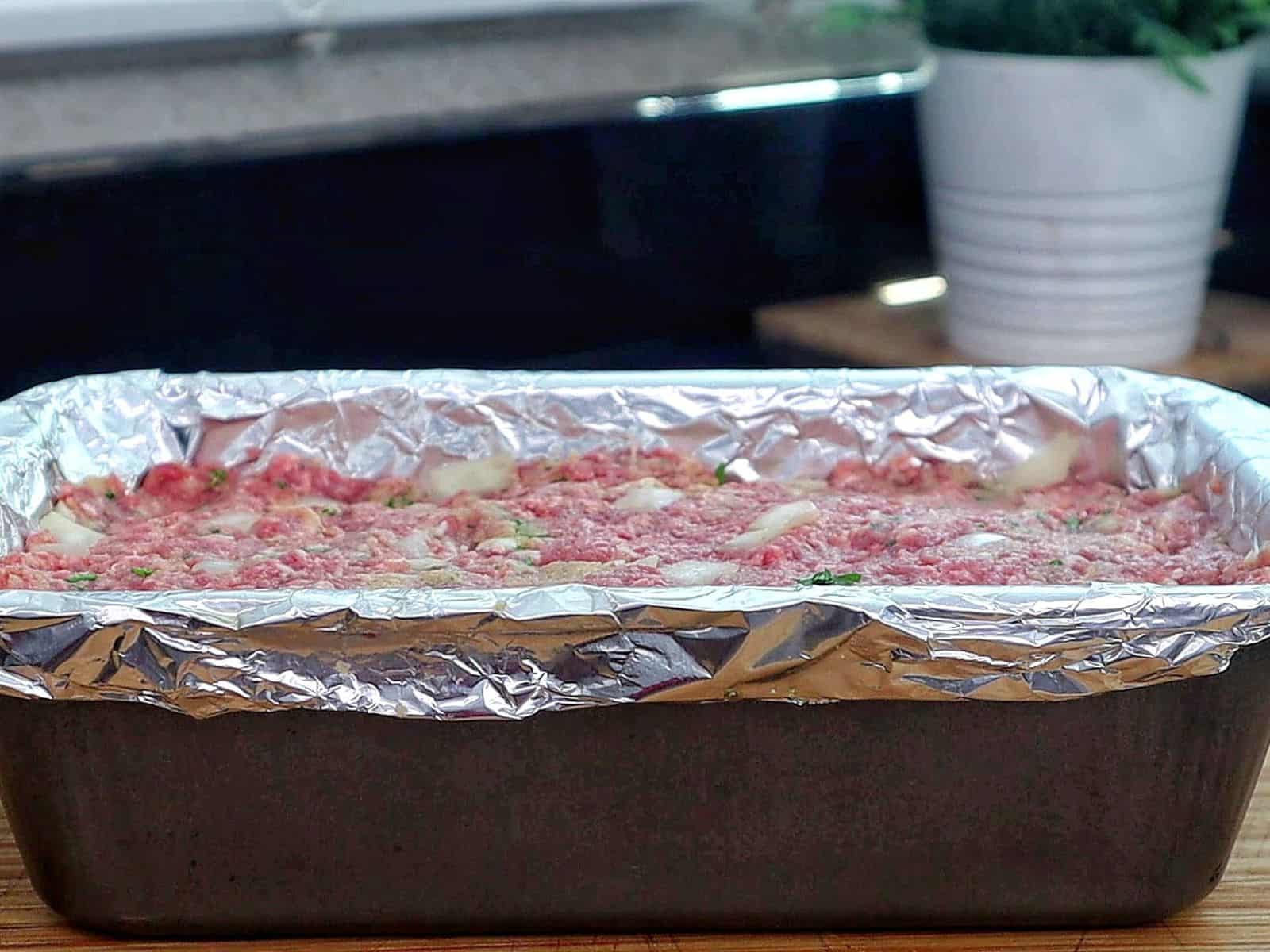 A thick slice of garlic parmesan meatloaf topped with a creamy garlic parmesan sauce and fresh parsley, served on a wooden cutting board with a juicy, tender center visible in every bite.