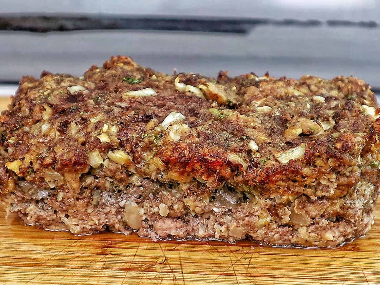 A thick slice of garlic parmesan meatloaf topped with a creamy garlic parmesan sauce and fresh parsley, served on a wooden cutting board with a juicy, tender center visible in every bite.