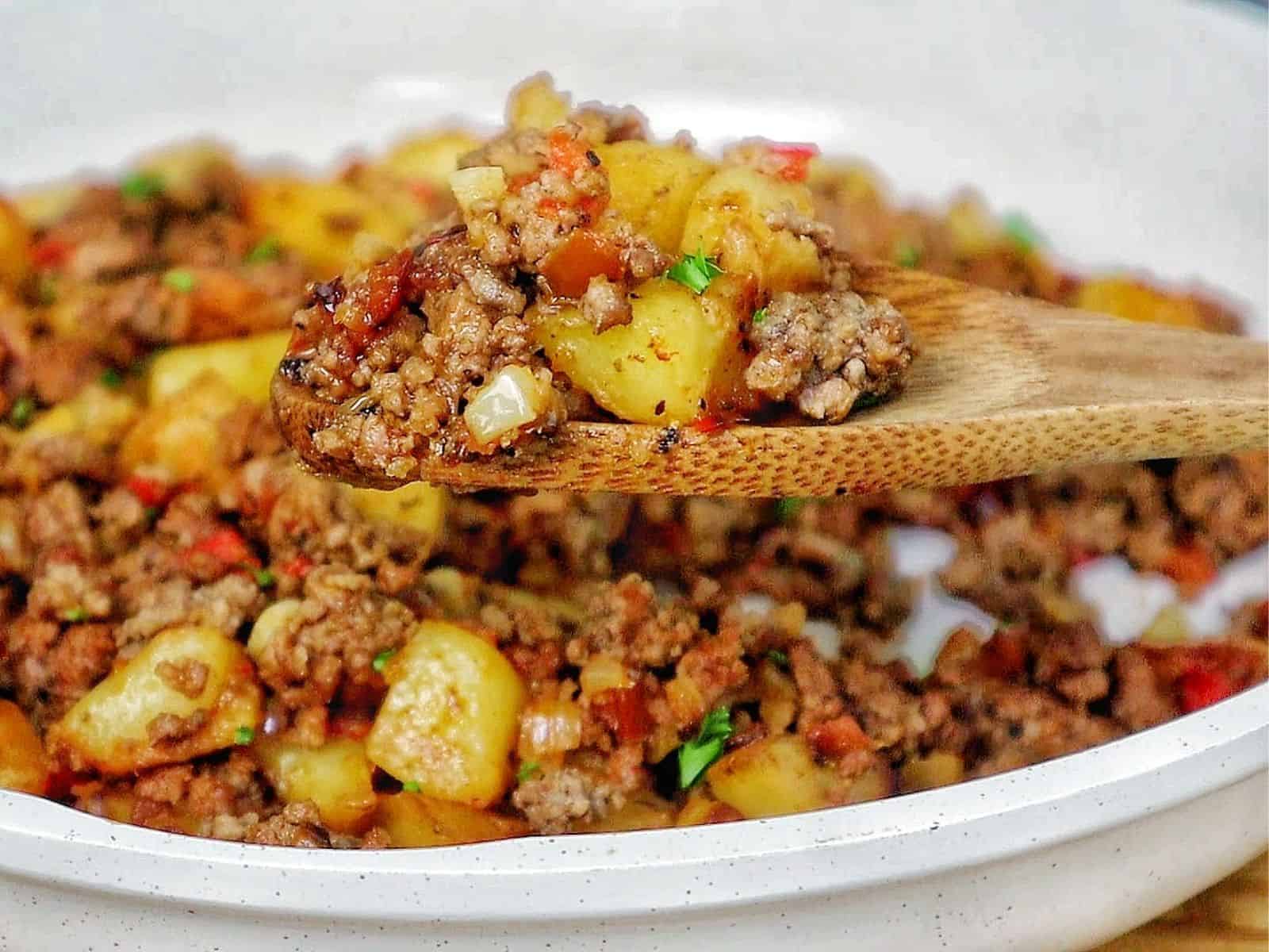 A bowl of homemade hamburger hash filled with seasoned ground beef, crispy golden potatoes, diced red peppers, onions, and herbs.