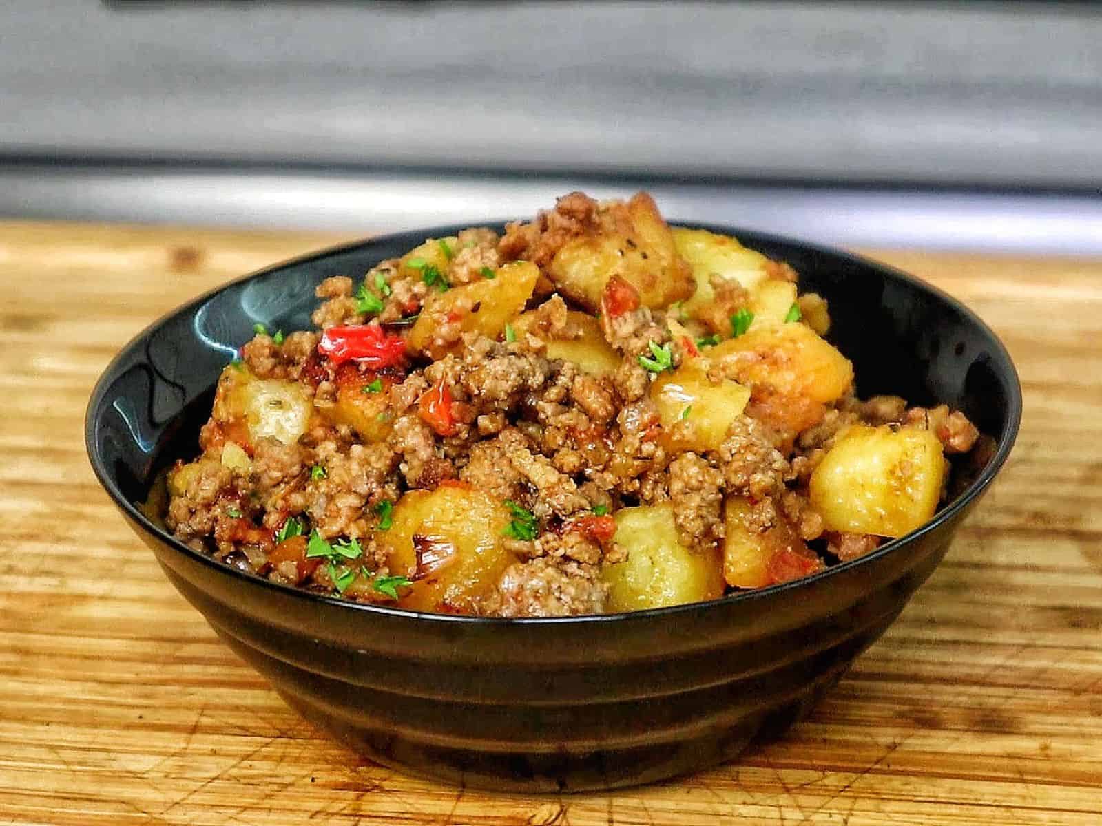A bowl of homemade hamburger hash filled with seasoned ground beef, crispy golden potatoes, diced red peppers, onions, and herbs. 