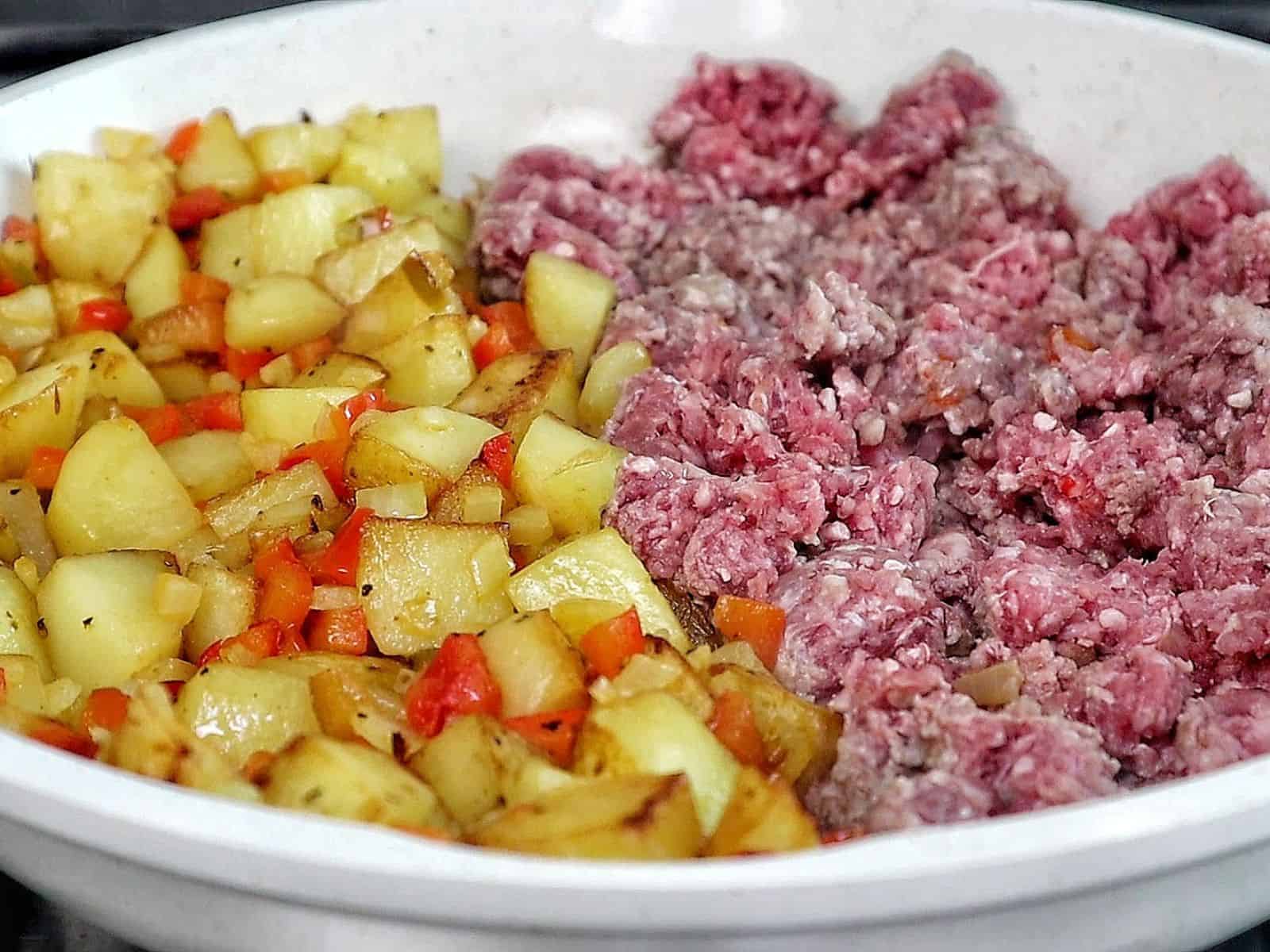 A bowl of homemade hamburger hash filled with seasoned ground beef, crispy golden potatoes, diced red peppers, onions, and herbs.