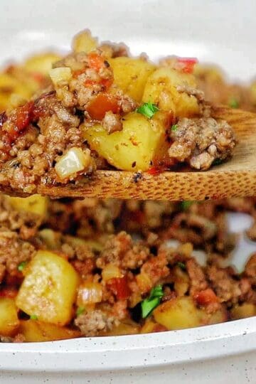 A bowl of homemade hamburger hash filled with seasoned ground beef, crispy golden potatoes, diced red peppers, onions, and herbs.