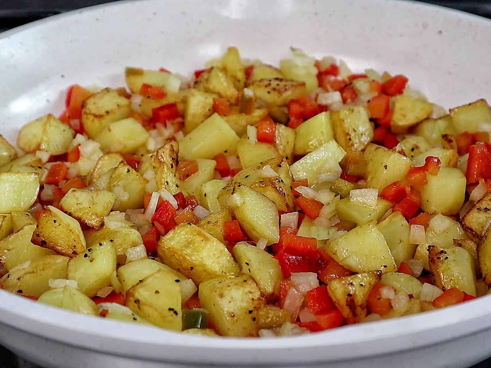 A bowl of homemade hamburger hash filled with seasoned ground beef, crispy golden potatoes, diced red peppers, onions, and herbs.