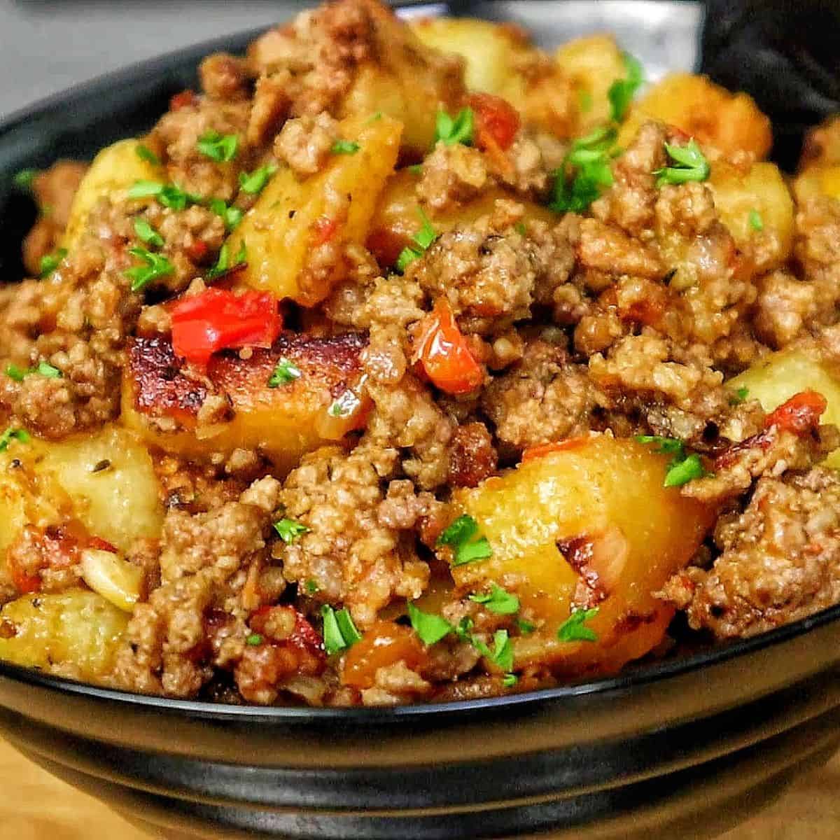 A bowl of homemade hamburger hash filled with seasoned ground beef, crispy golden potatoes, diced red peppers, onions, and herbs.