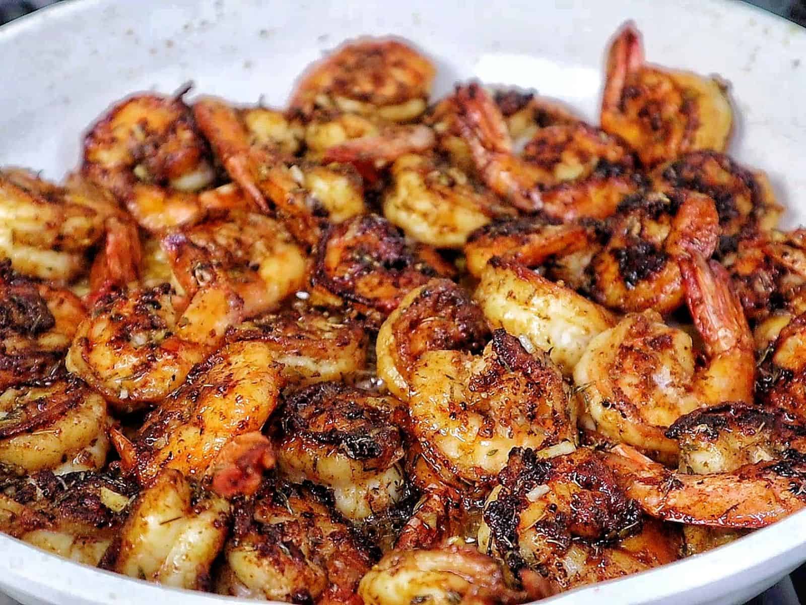 Bowl of hot honey garlic shrimp coated in a glossy sweet and spicy sauce, garnished with parsley.
