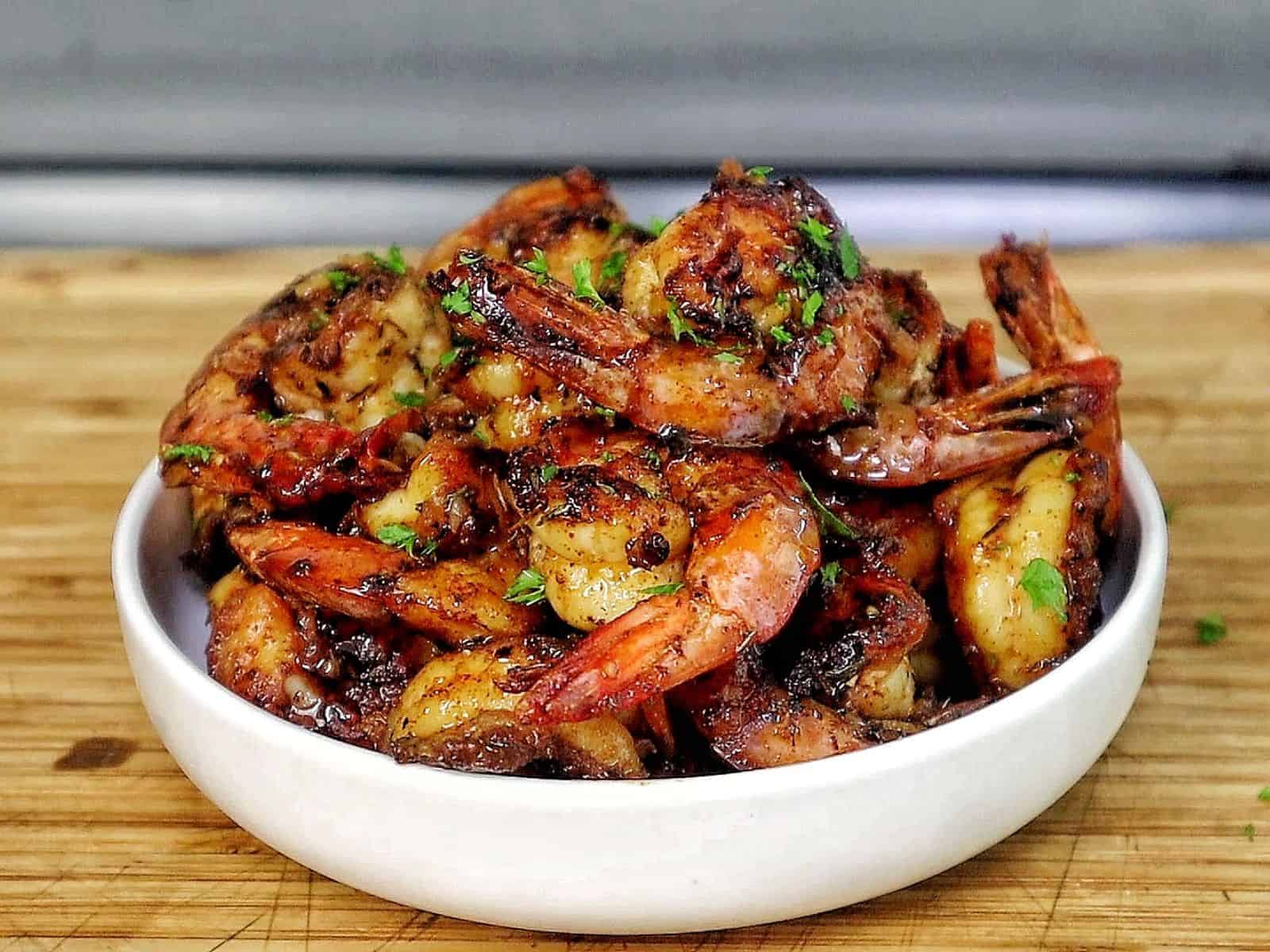 Bowl of hot honey garlic shrimp coated in a glossy sweet and spicy sauce, garnished with parsley.