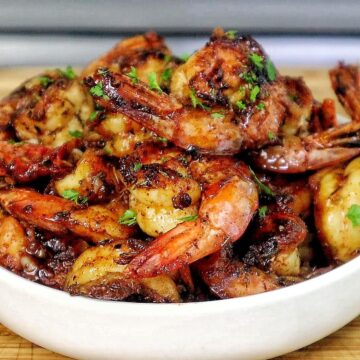 Bowl of hot honey garlic shrimp coated in a glossy sweet and spicy sauce, garnished with parsley.