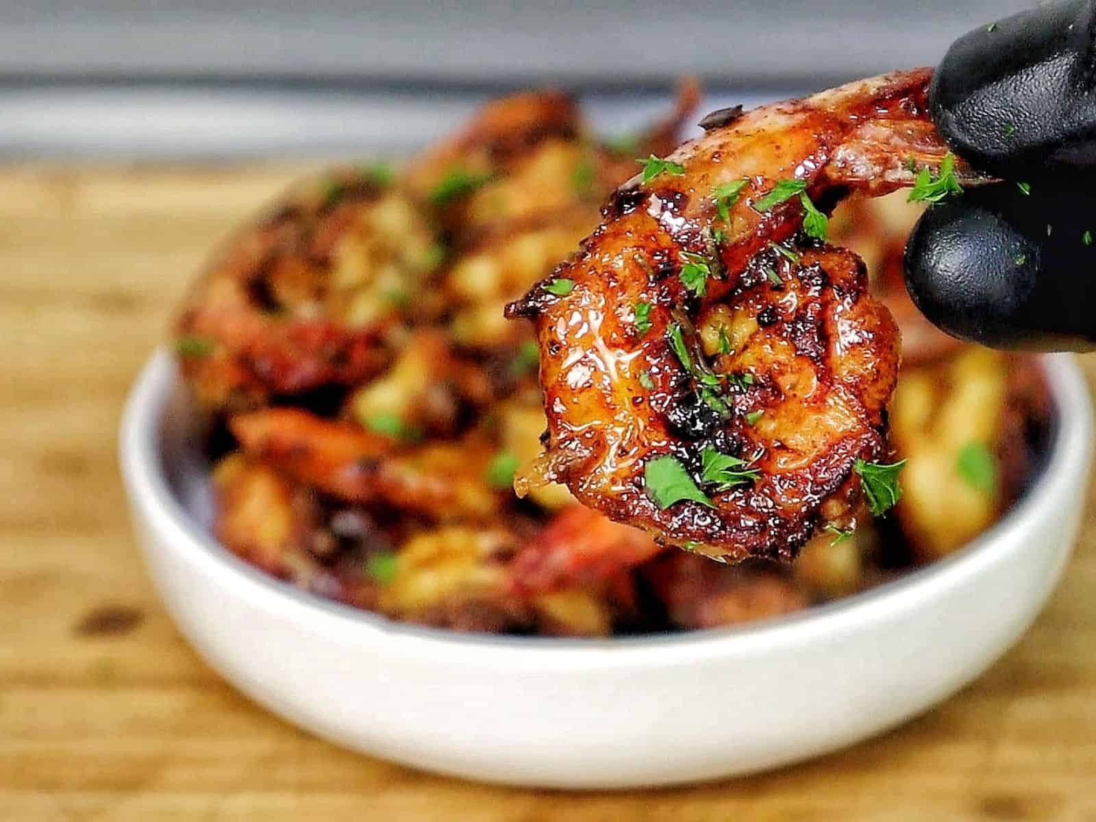Bowl of hot honey garlic shrimp coated in a glossy sweet and spicy sauce, garnished with parsley.