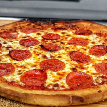 Homemade pepperoni pizza with melted mozzarella and crispy buffalo wings cooked in a pellet pizza oven, served hot with charred crust and golden wings