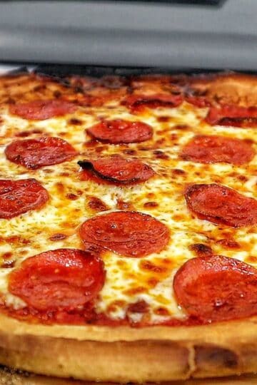 Homemade pepperoni pizza with melted mozzarella and crispy buffalo wings cooked in a pellet pizza oven, served hot with charred crust and golden wings