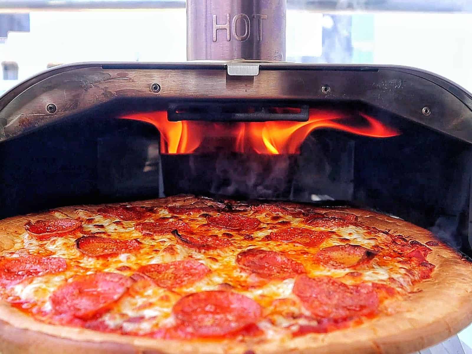 Homemade pepperoni pizza with melted mozzarella and crispy buffalo wings cooked in a pellet pizza oven, served hot with charred crust and golden wings.