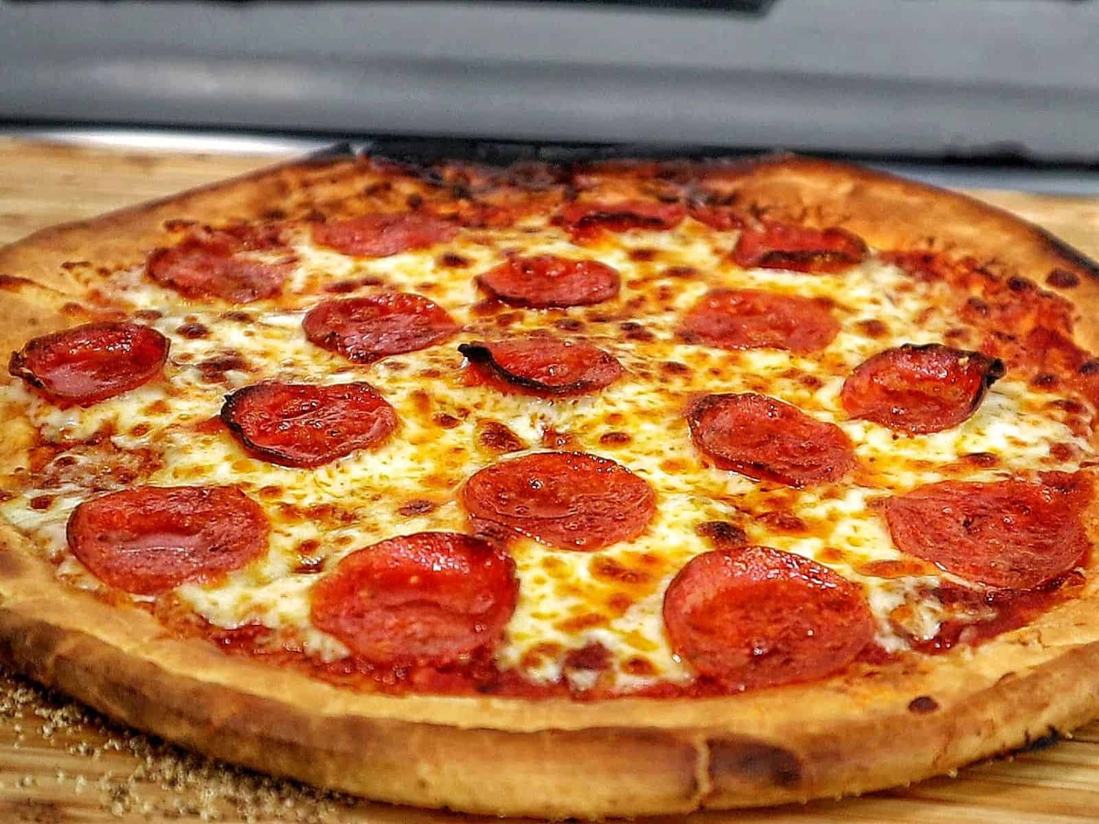 Homemade pepperoni pizza with melted mozzarella and crispy buffalo wings cooked in a pellet pizza oven, served hot with charred crust and golden wings.
