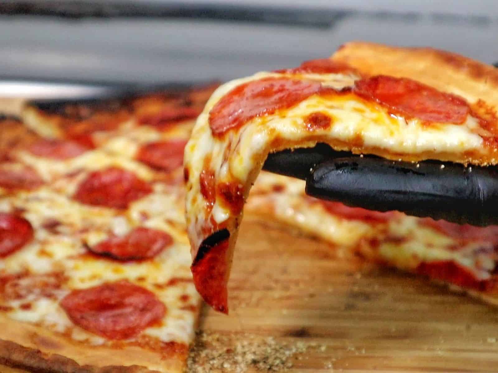 Homemade pepperoni pizza with melted mozzarella and crispy buffalo wings cooked in a pellet pizza oven, served hot with charred crust and golden wings.
