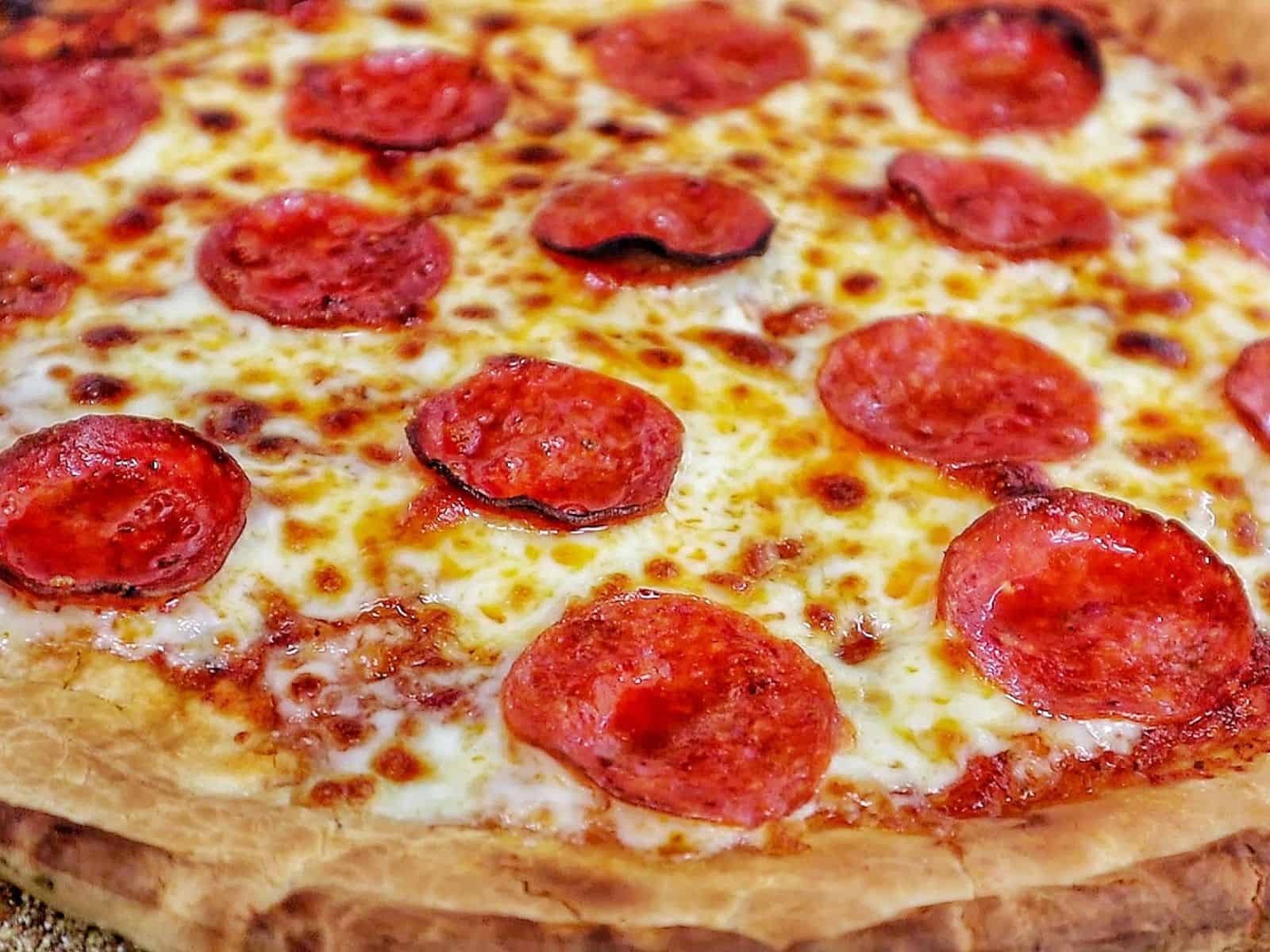 Homemade pepperoni pizza with melted mozzarella and crispy buffalo wings cooked in a pellet pizza oven, served hot with charred crust and golden wings.