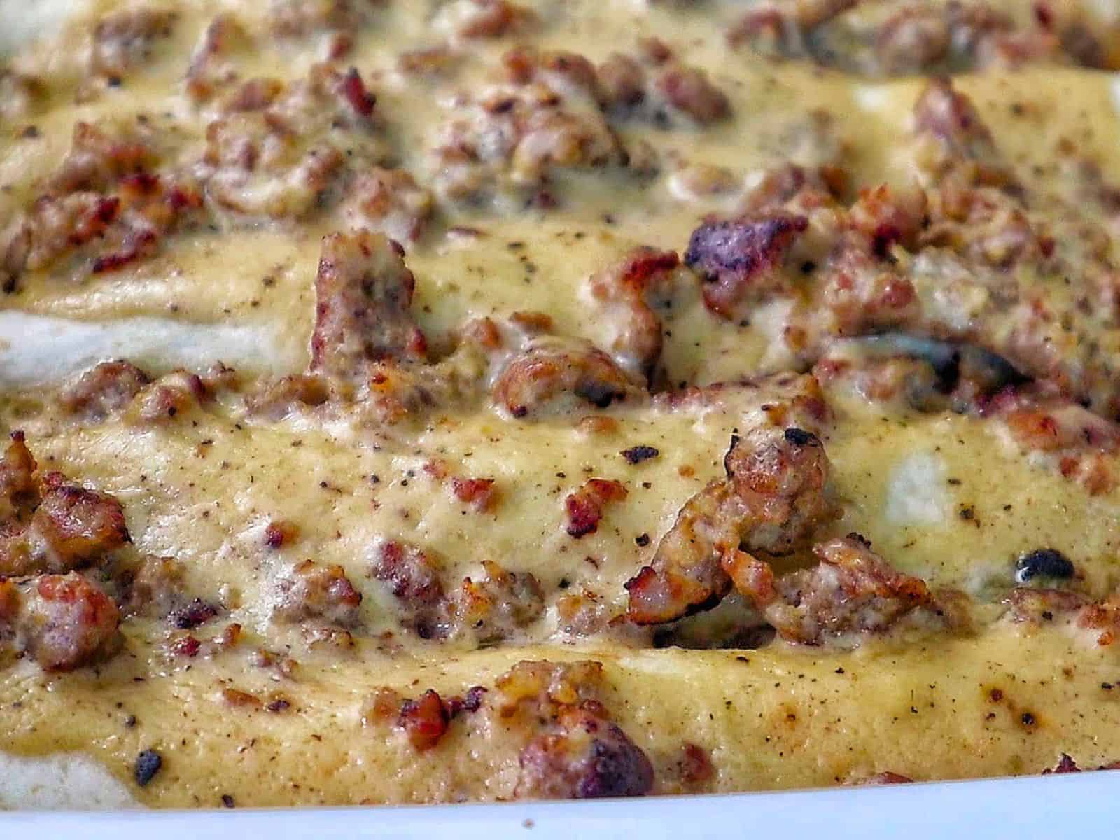 Breakfast enchiladas topped with creamy homemade sausage gravy and melted cheese. The enchiladas are stuffed with scrambled eggs, sausage, hash browns, and cheese.