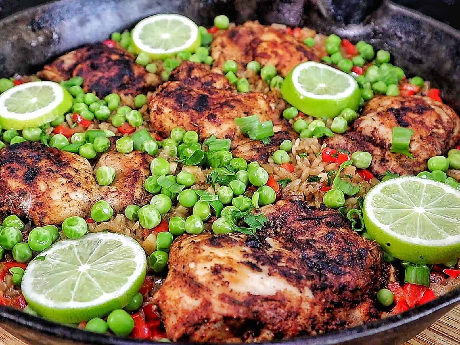 Caribbean-style chicken and rice, nestled in fluffy rice with red bell peppers, green peas, sliced green onions, and fresh lime rounds for garnish.