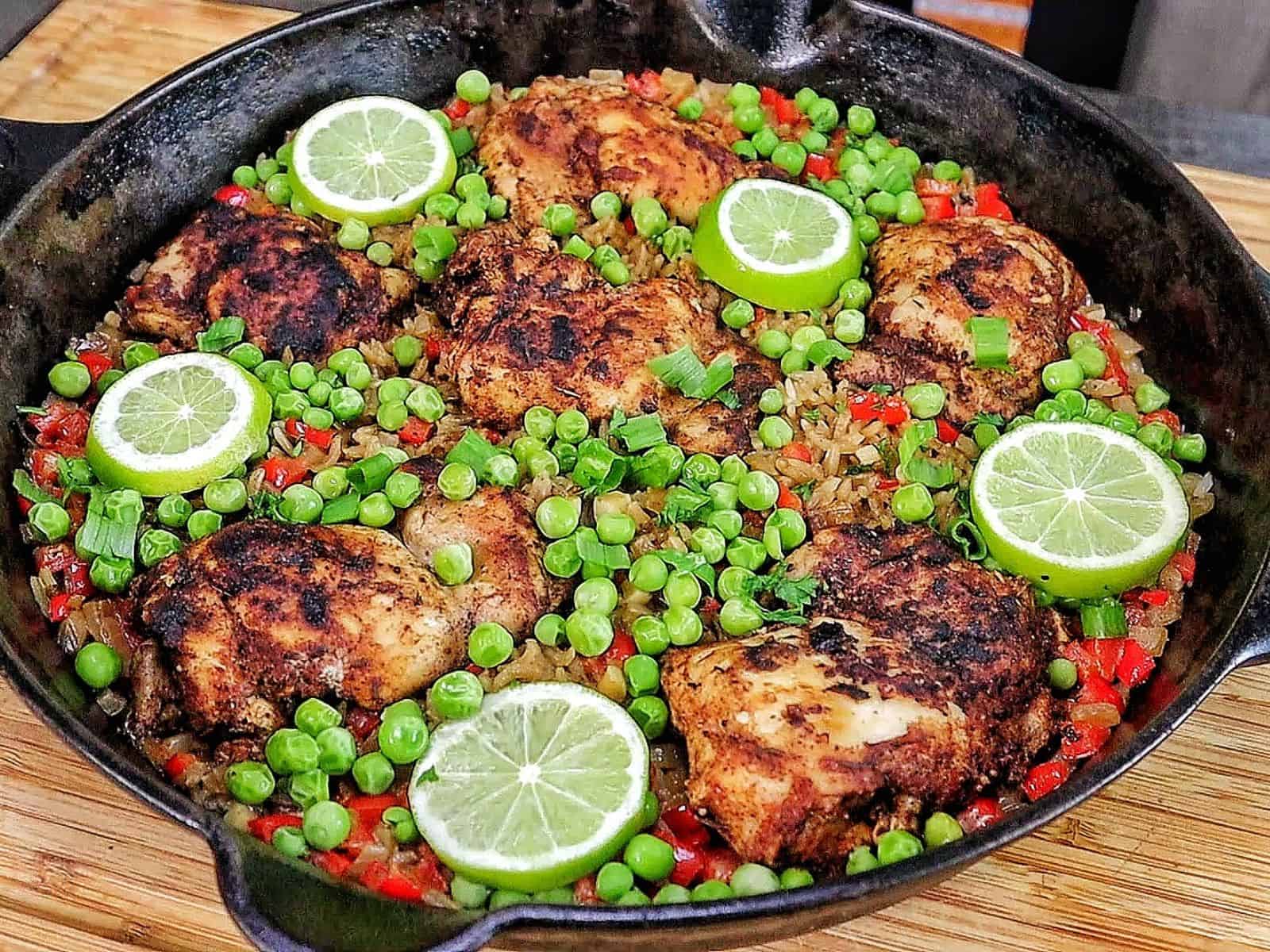 Caribbean-style chicken and rice, nestled in fluffy rice with red bell peppers, green peas, sliced green onions, and fresh lime rounds for garnish.