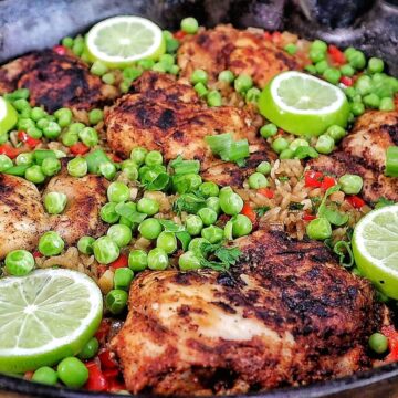 Caribbean-style chicken and rice, nestled in fluffy rice with red bell peppers, green peas, sliced green onions, and fresh lime rounds for garnish.