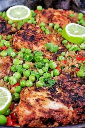 Caribbean-style chicken and rice, nestled in fluffy rice with red bell peppers, green peas, sliced green onions, and fresh lime rounds for garnish.