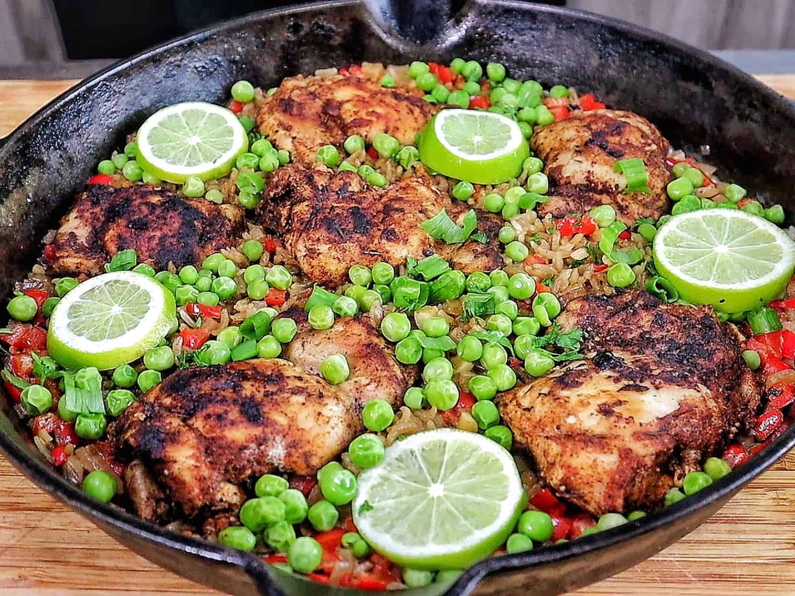 Caribbean-style chicken and rice, nestled in fluffy rice with red bell peppers, green peas, sliced green onions, and fresh lime rounds for garnish.