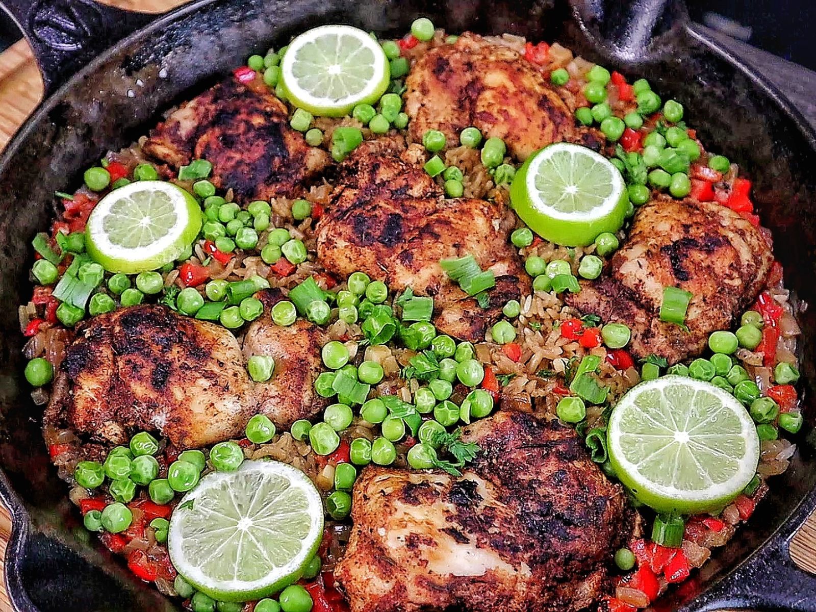 Caribbean-style chicken and rice, nestled in fluffy rice with red bell peppers, green peas, sliced green onions, and fresh lime rounds for garnish.