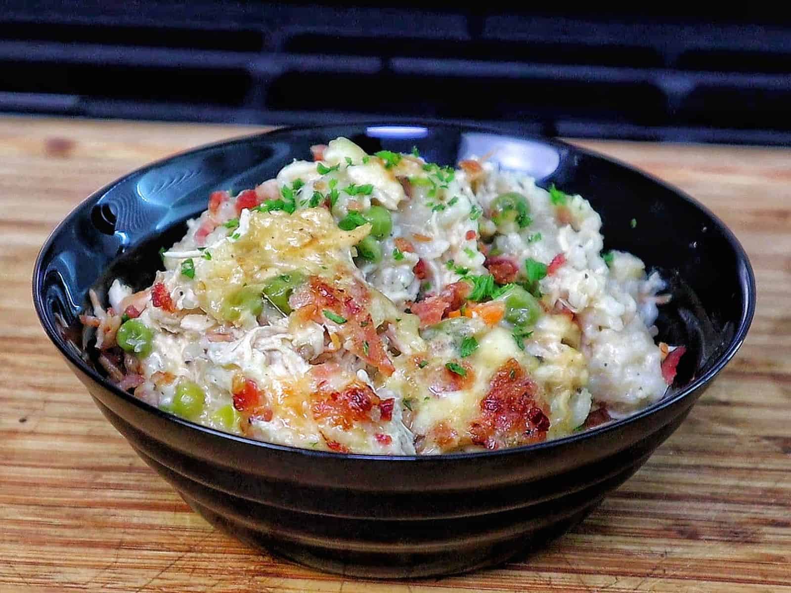 Creamy Chicken Alfredo Rice Casserole baked until golden and bubbly in a casserole dish, loaded with tender shredded chicken, peas, carrots, crispy bacon, melted mozzarella cheese, and a rich Alfredo sauce, garnished with fresh parsley.