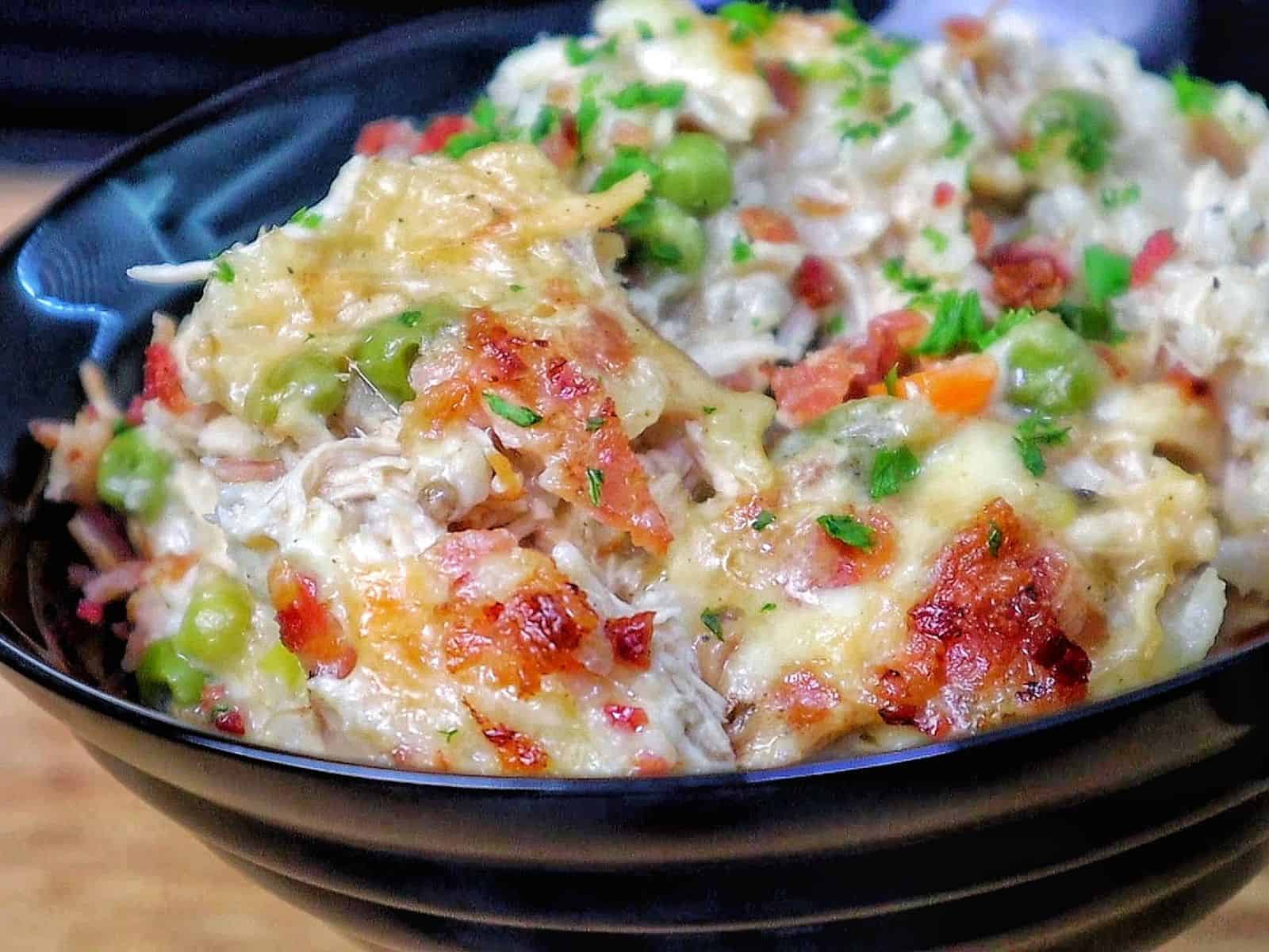 Creamy Chicken Alfredo Rice Casserole baked until golden and bubbly in a casserole dish, loaded with tender shredded chicken, peas, carrots, crispy bacon, melted mozzarella cheese, and a rich Alfredo sauce, garnished with fresh parsley.