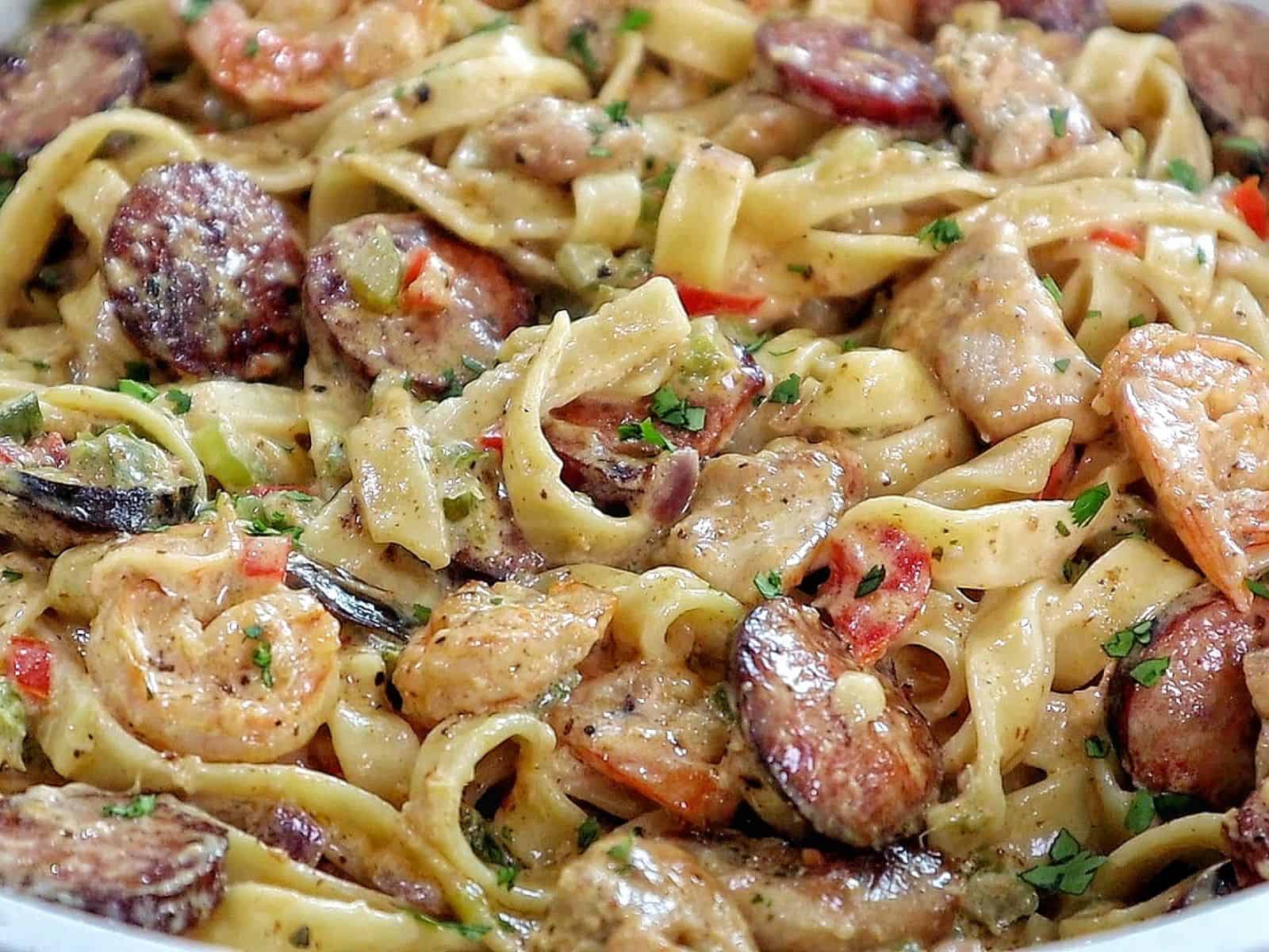 Creamy jambalaya pasta loaded with Cajun-seasoned shrimp, tender chicken thighs, smoked sausage, fettuccine noodles, peppers, celery, onions, and Parmesan cream sauce, garnished with fresh parsley.