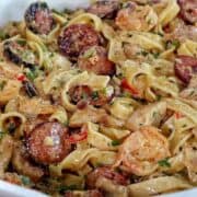 Creamy jambalaya pasta loaded with Cajun-seasoned shrimp, tender chicken thighs, smoked sausage, fettuccine noodles, peppers, celery, onions, and Parmesan cream sauce, garnished with fresh parsley.