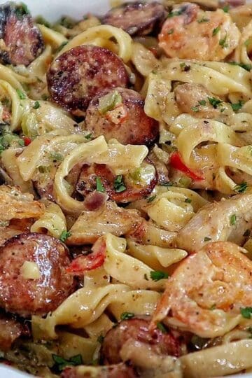 Creamy jambalaya pasta loaded with Cajun-seasoned shrimp, tender chicken thighs, smoked sausage, fettuccine noodles, peppers, celery, onions, and Parmesan cream sauce, garnished with fresh parsley.