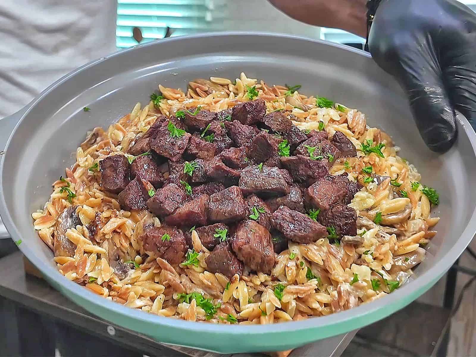 A bowl of creamy Parmesan mushroom orzo topped with perfectly seared steak bites and garnished with fresh parsley