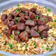 A bowl of creamy Parmesan mushroom orzo topped with perfectly seared steak bites and garnished with fresh parsley