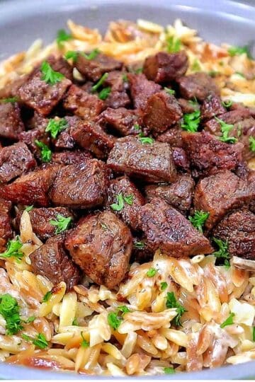 A bowl of creamy Parmesan mushroom orzo topped with perfectly seared steak bites and garnished with fresh parsley