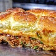 Baked BBQ chicken sliders made with Hawaiian rolls, shredded BBQ chicken, melted Gouda cheese, diced red onion, and cilantro, brushed with garlic herb butter.