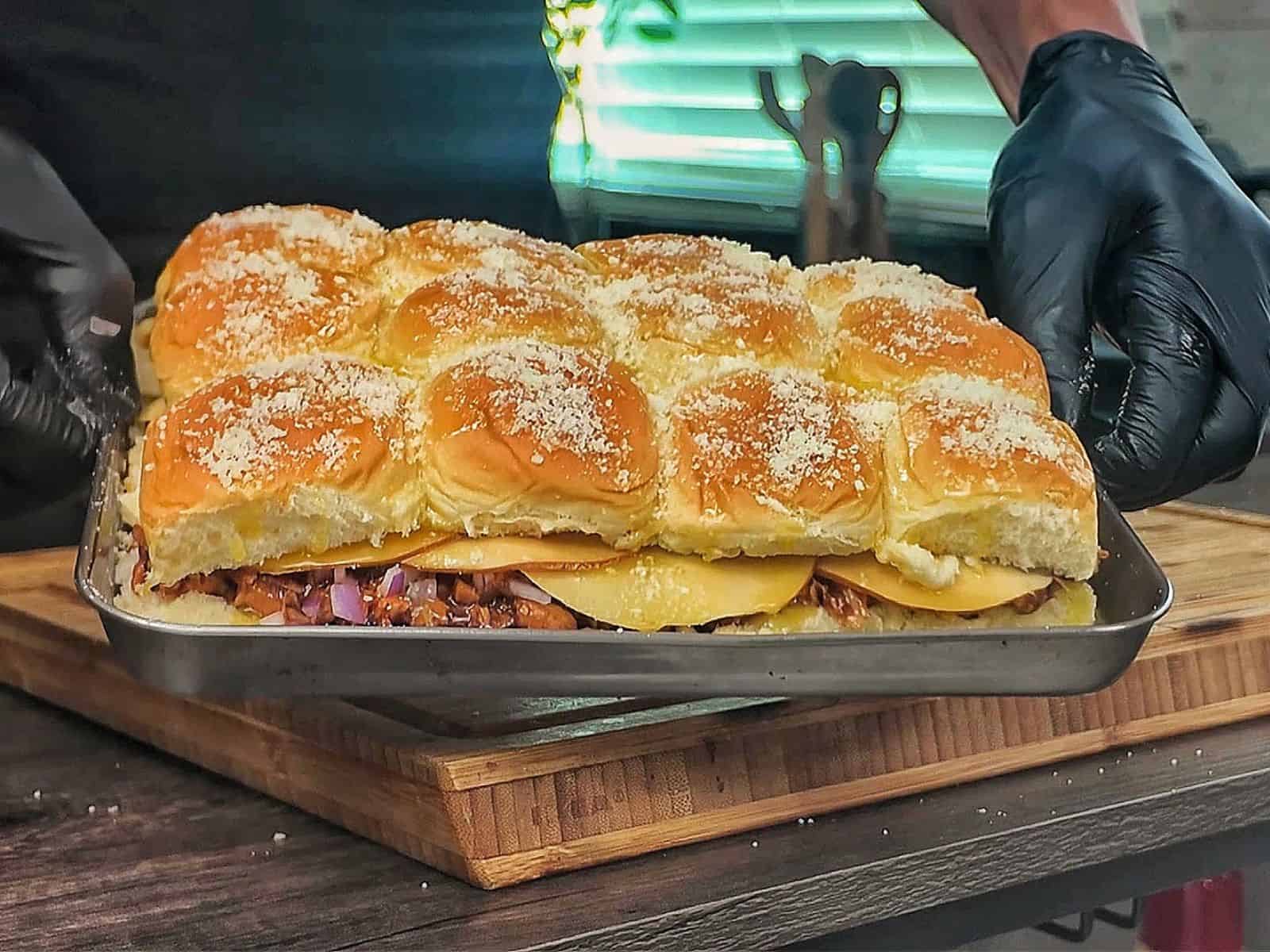 Baked BBQ chicken sliders made with Hawaiian rolls, shredded BBQ chicken, melted Gouda cheese, diced red onion, and cilantro, brushed with garlic herb butter.
