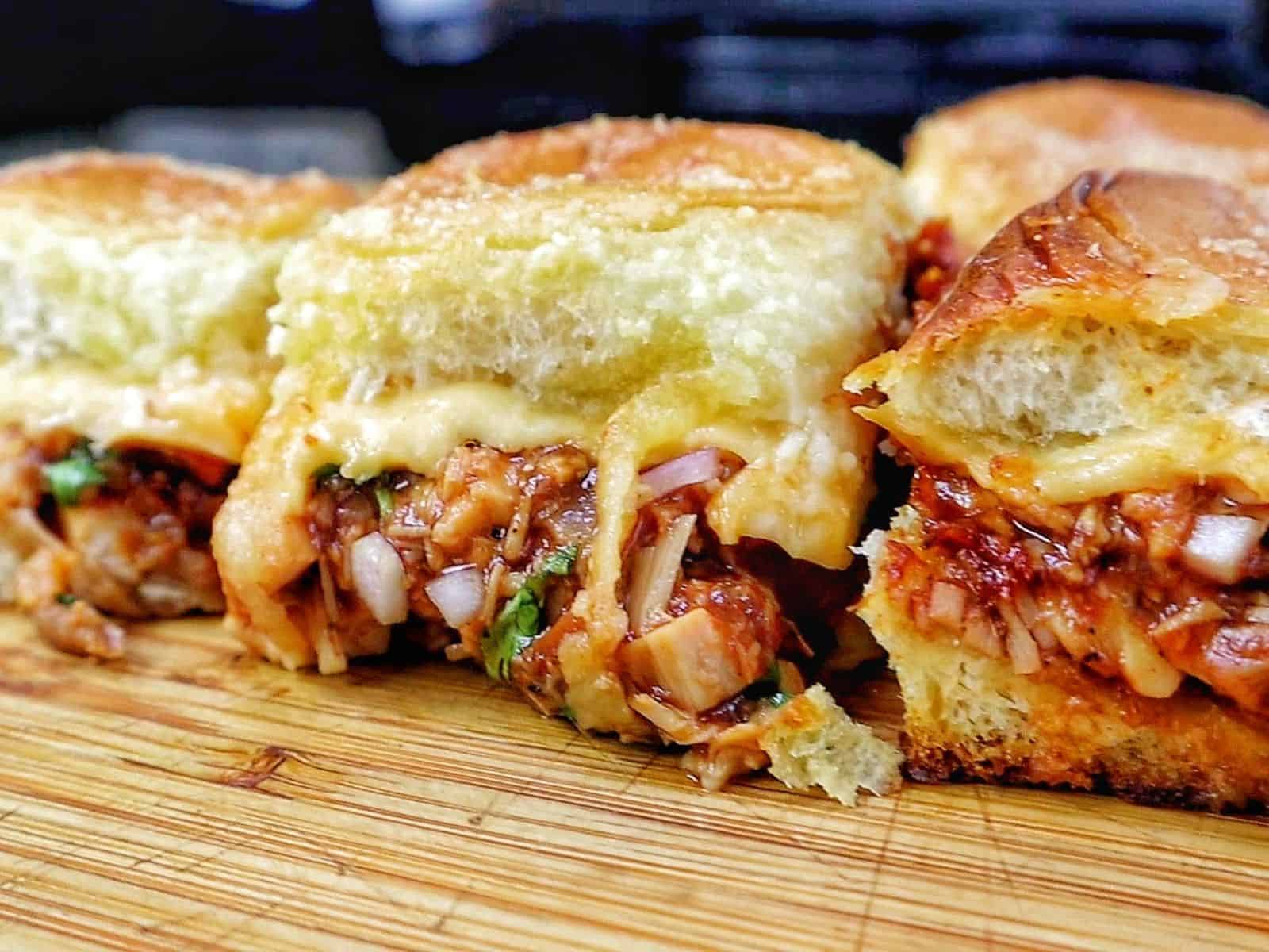 Baked BBQ chicken sliders made with Hawaiian rolls, shredded BBQ chicken, melted Gouda cheese, diced red onion, and cilantro, brushed with garlic herb butter.