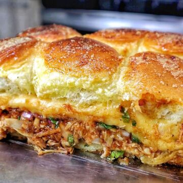 Baked BBQ chicken sliders made with Hawaiian rolls, shredded BBQ chicken, melted Gouda cheese, diced red onion, and cilantro, brushed with garlic herb butter.