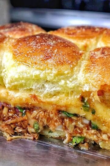 Baked BBQ chicken sliders made with Hawaiian rolls, shredded BBQ chicken, melted Gouda cheese, diced red onion, and cilantro, brushed with garlic herb butter.