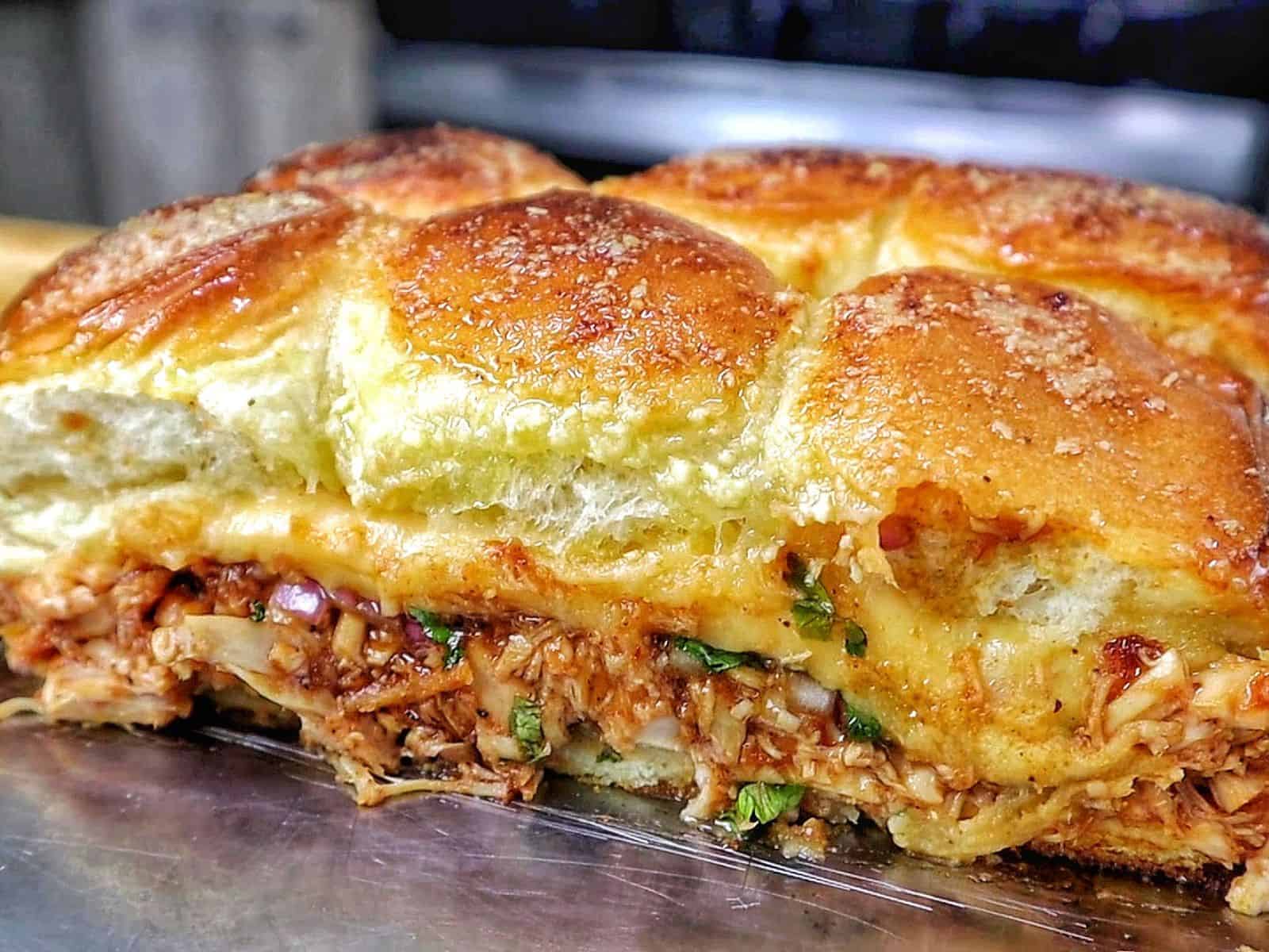 Baked BBQ chicken sliders made with Hawaiian rolls, shredded BBQ chicken, melted Gouda cheese, diced red onion, and cilantro, brushed with garlic herb butter.